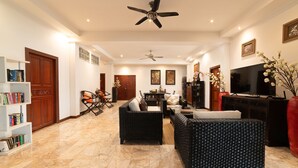 A spacious living room with a high ceiling fan, a television, and a large bookshelf. - Lumaya Rawai (Rawai)