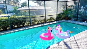 Una piscina con dos cisnes inflables, rodeada por una zona cubierta con vista a un barrio residencial.