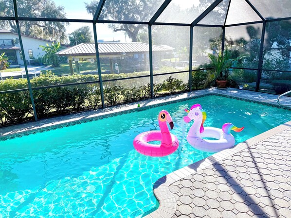 A swimming pool with two inflatable swans, surrounded by a covered area with a view of a residential neighborhood.