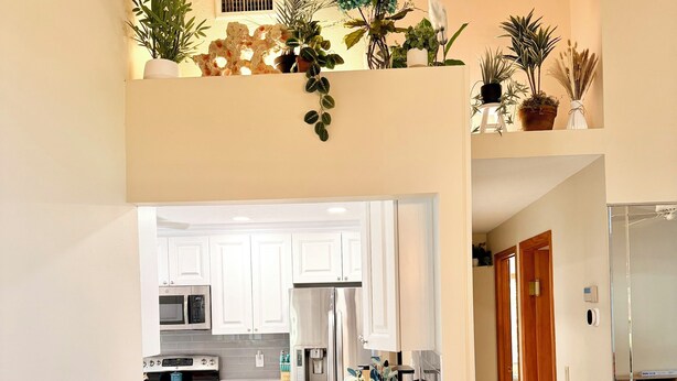 Una cocina moderna con armarios blancos, horno integrado y refrigerador. Hay dos taburetes de mimbre y un florero con flores en la encimera.