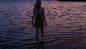 Una persona de pie a la orilla del agua al atardecer.