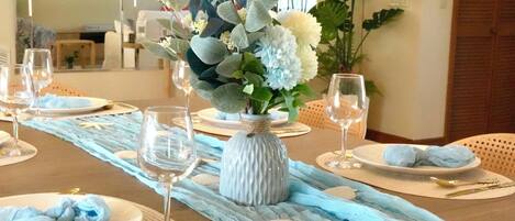 Una mesa de comedor dispuesta con platos, vasos y un centro de mesa con flores y un florero.