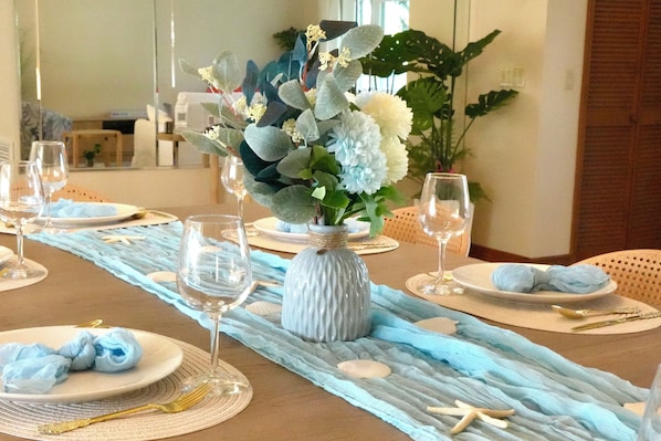 Una mesa de comedor dispuesta con platos, vasos y un centro de mesa con flores y un florero.