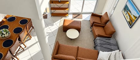 A spacious living area with a view of the ocean, a dining table with woven placemats, and a modern sofa set.