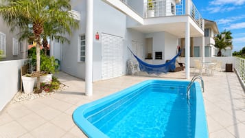 Una piscina con borde azul, rodeada por un edificio blanco con balcones y plantas en macetas.
