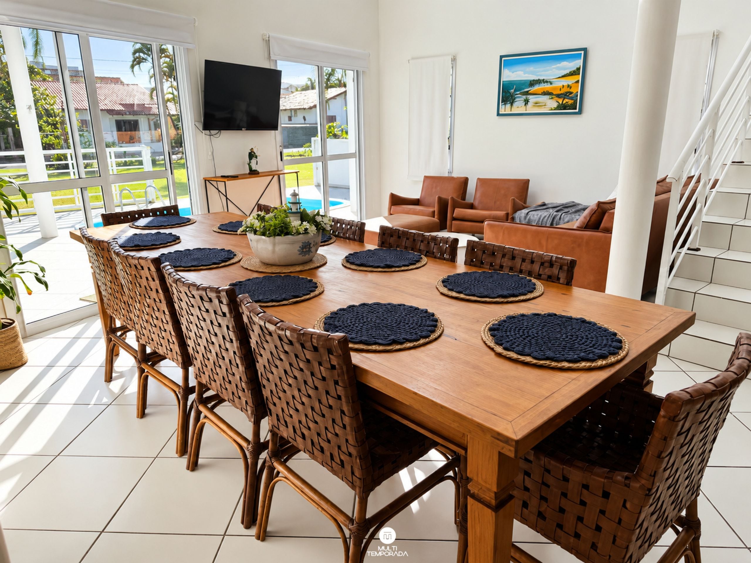 Un comedor con una mesa de madera, sillas tejidas y vistas al exterior.