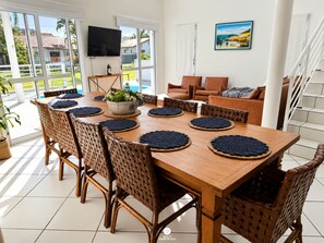 Un comedor con una mesa de madera, sillas tejidas y vistas al exterior.