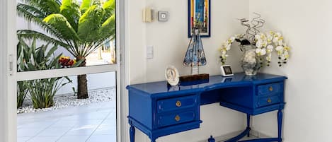 A blue desk with drawers, a framed picture, and a vase with white flowers.