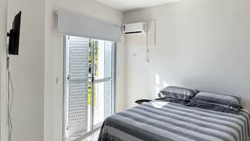 Un dormitorio con cama, ventilador de techo, equipo de aire acondicionado y puerta corrediza de vidrio.