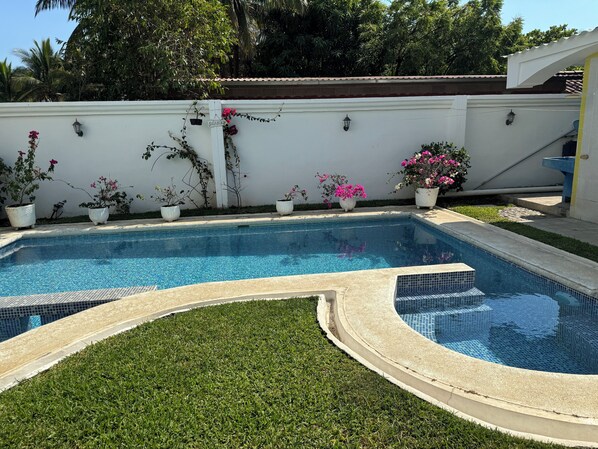 Piscina retangular com borda em azulejo, rodeada por um gramado bem cuidado e plantas em vasos.