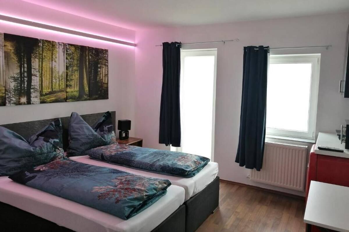 A bedroom with two beds, a nightstand, a desk, and a window with curtains.