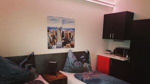 A bedroom with two single beds, a nightstand with a speaker, a red cabinet, and a cityscape painting on the wall. - Motel Graz Ost  (Graz)