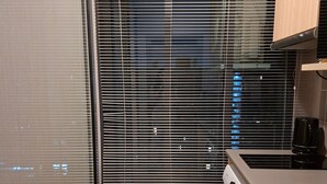 A compact kitchen with a washing machine, a coffee maker, and a view through a window with blinds.
