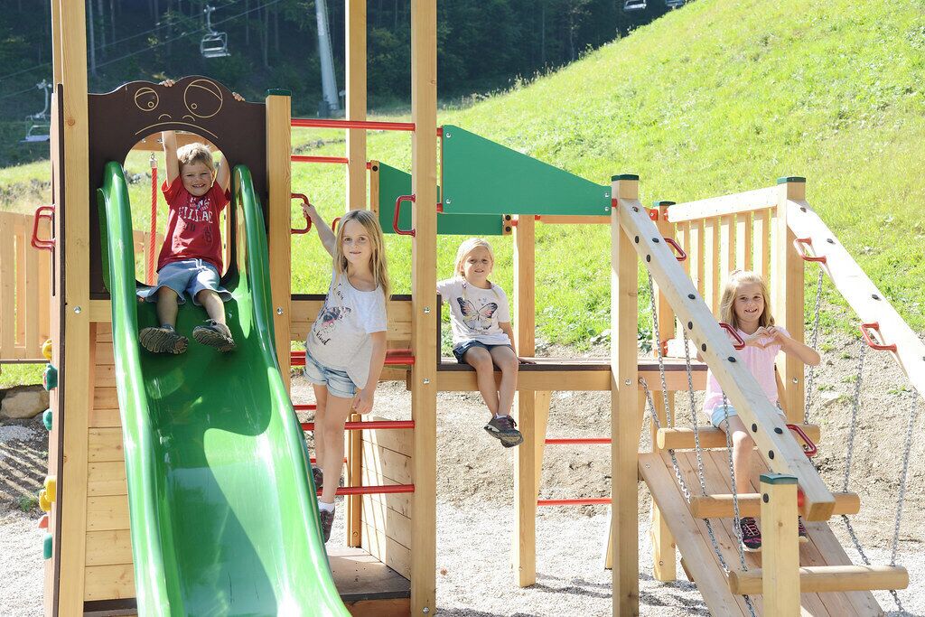 Une aire de jeux avec un toboggan vert, des structures d’escalade et un espace de jeux en bois.