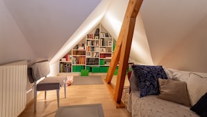 A cozy attic room with a sloped ceiling, a wooden chair, a sofa, a bookshelf, and a radiator. - Guest Room in Laroin for 2 to 4 Guests – Nature and Tranquility Await (Laroin)
