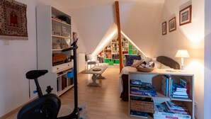 A room with a ceiling fan, exercise bike, bookshelves, a dining table, and a lamp. - Guest Room in Laroin for 2 to 4 Guests – Nature and Tranquility Await (Laroin)