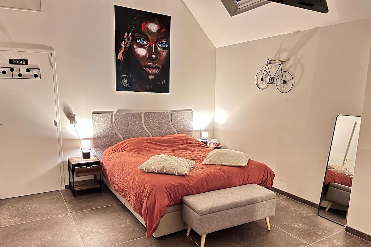 A bedroom with a bed, bedside tables, a mirror, and a wall-mounted bicycle.