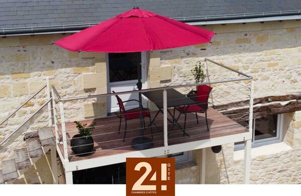 Un balcon avec un parasol rouge, une table et deux chaises.
