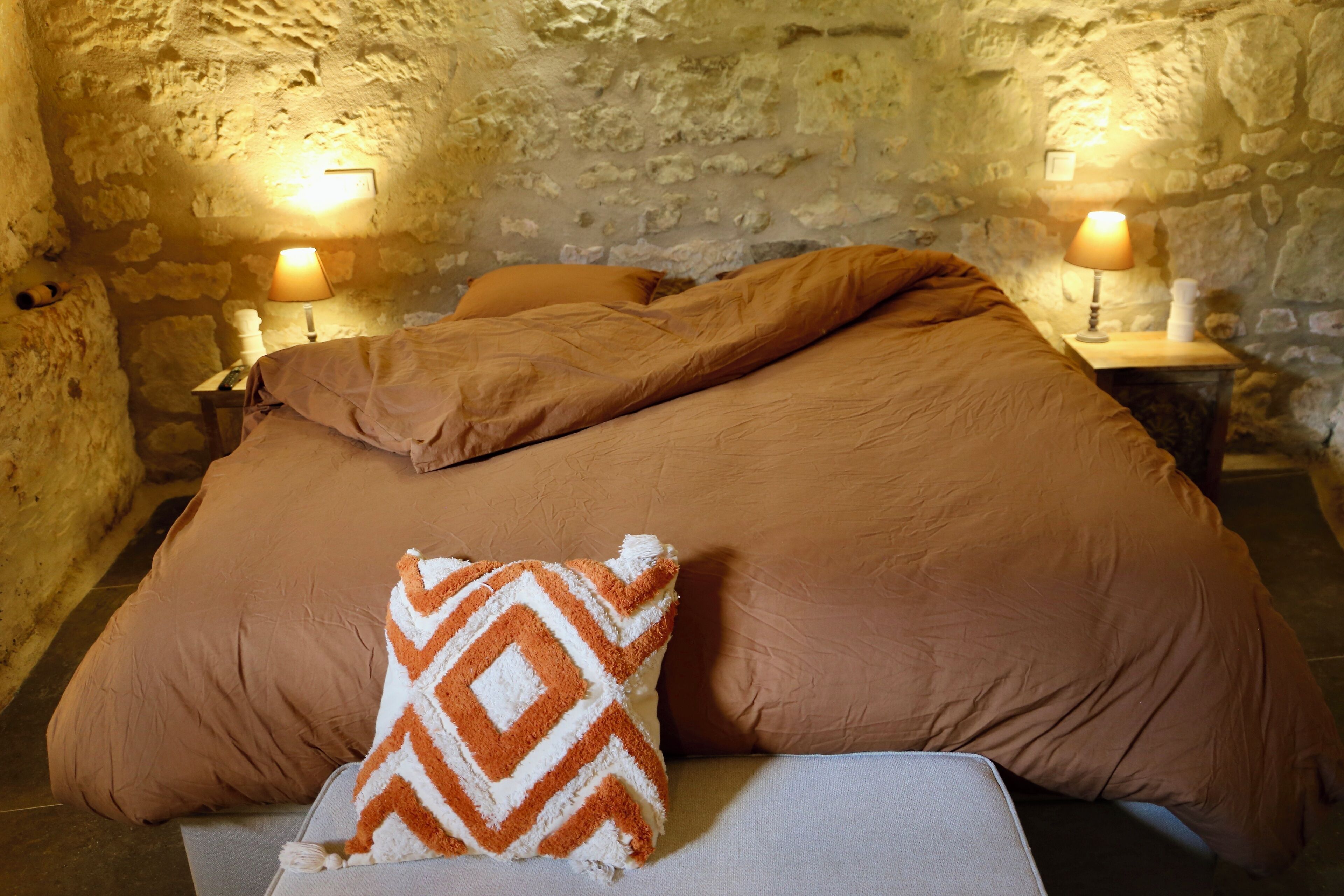 A bedroom with a large bed, two bedside lamps, and a stone wall.