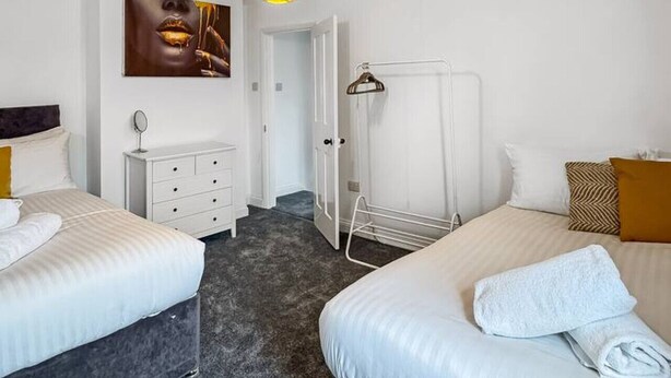 A hotel room with two beds, a white dresser, a mirror, a painting on the wall, and a hanging light fixture.