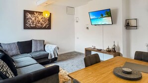 A modern living room with a sofa, a dining table, a TV, and a ceiling light.