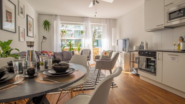 A modern kitchen with white cabinets, a built-in oven, and a dining area with a round table and chairs. - Special *PRIMERO PICASSO* Apartment (Basel)