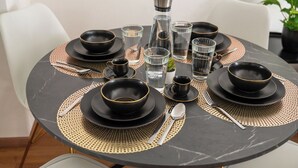 A round dining table set with black plates, bowls, and glasses, accompanied by gold-rimmed cutlery and a water pitcher. - Special *PRIMERO PICASSO* Apartment (Basel)