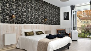 A bedroom with a bed, two wall sconces, a radiator, a window with a view, and a black and white patterned wallpaper.