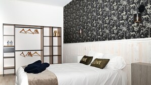 A bedroom with a bed, a wardrobe, a shelf with bottles, and a wall with a floral pattern.