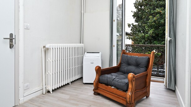 Ein Balkon mit Heizkörper, Stuhl und Fenster.