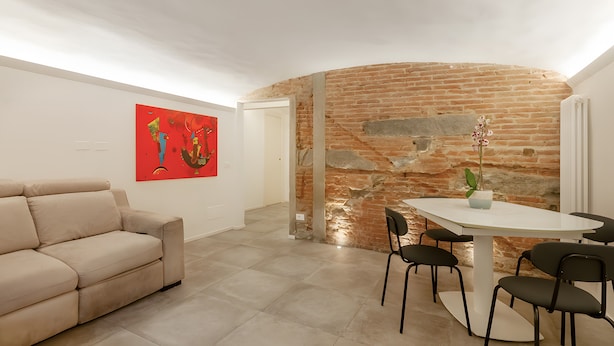 Ein modernes Wohnzimmer mit einer Couch, einem Esstisch mit Stühlen, einem roten abstrakten Gemälde und einer Ziegelwand.