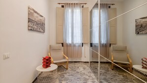 Ein Zimmer mit zwei Holzstühlen, einem kleinen runden Tisch, einem Spiegel und zwei Bildern an der Wand.