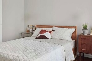 A neatly made bed with a quilted cover, a wooden headboard, and a bedside table with a lamp and books. - Vancouver Airport Inn (Richmond)