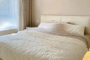 A bed with a headboard, a window with blinds, and a bedside table. - Vancouver Airport Inn (Richmond)