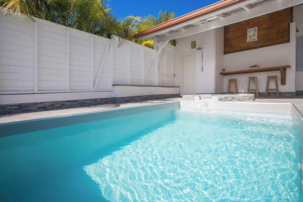 A swimming pool with a white wall and a wooden deck area.