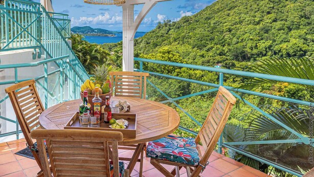 Een houten tafel met stoelen op een balkon met uitzicht op een weelderig groen landschap en een wateroppervlak.