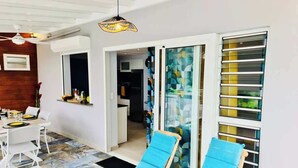 A modern room with a dining area, two blue lounge chairs, a ceiling fan, and a glass door leading to a balcony.