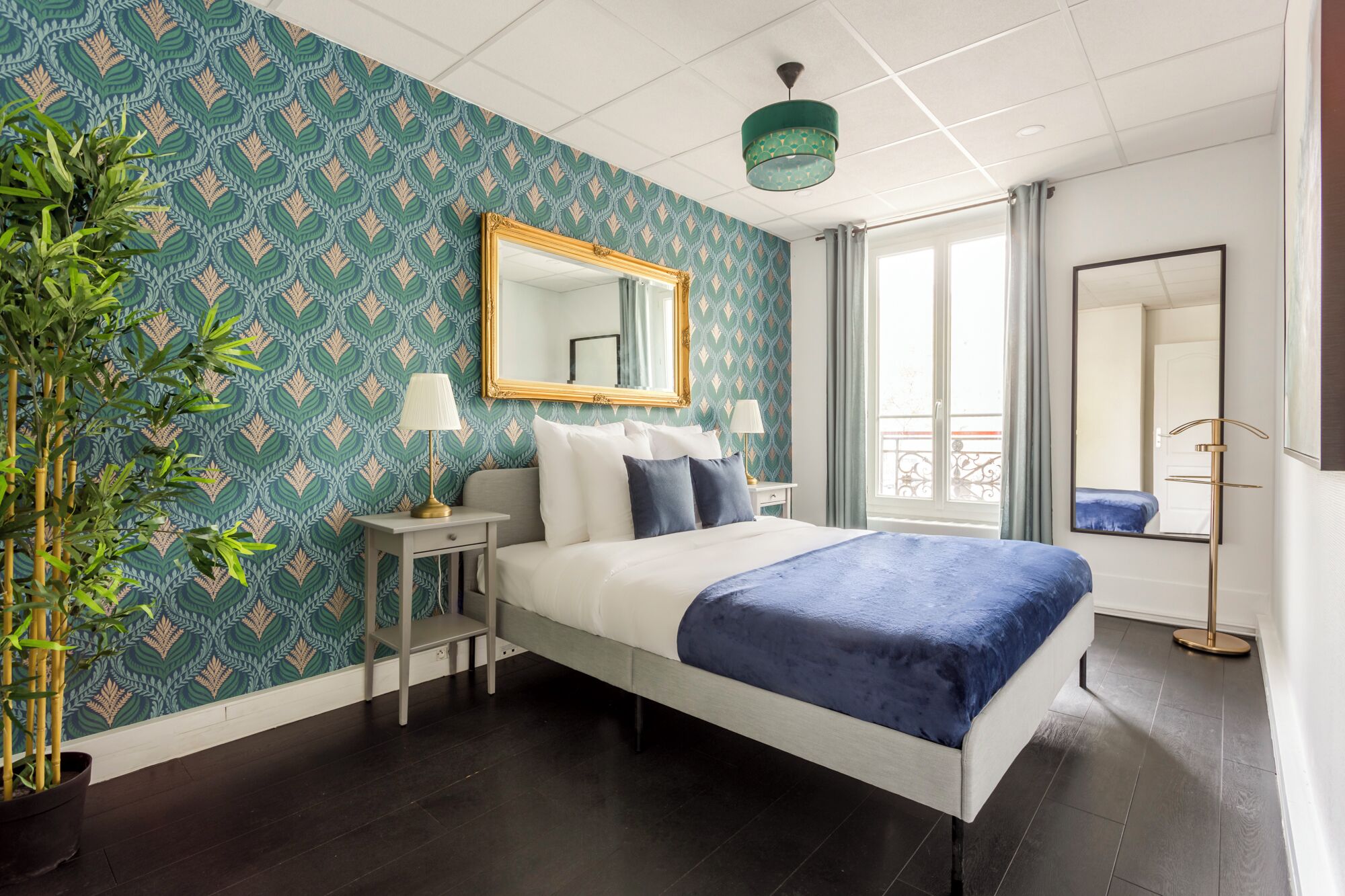 A bedroom with a bed, bedside tables, a mirror, a potted plant, and a view of the outside balcony.