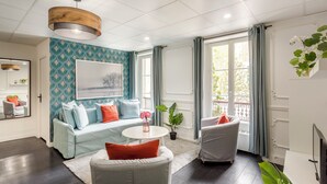 Een moderne woonkamer met een wand in teal met een patroon, een ronde witte salontafel, een grijze bank en een grijze fauteuil.