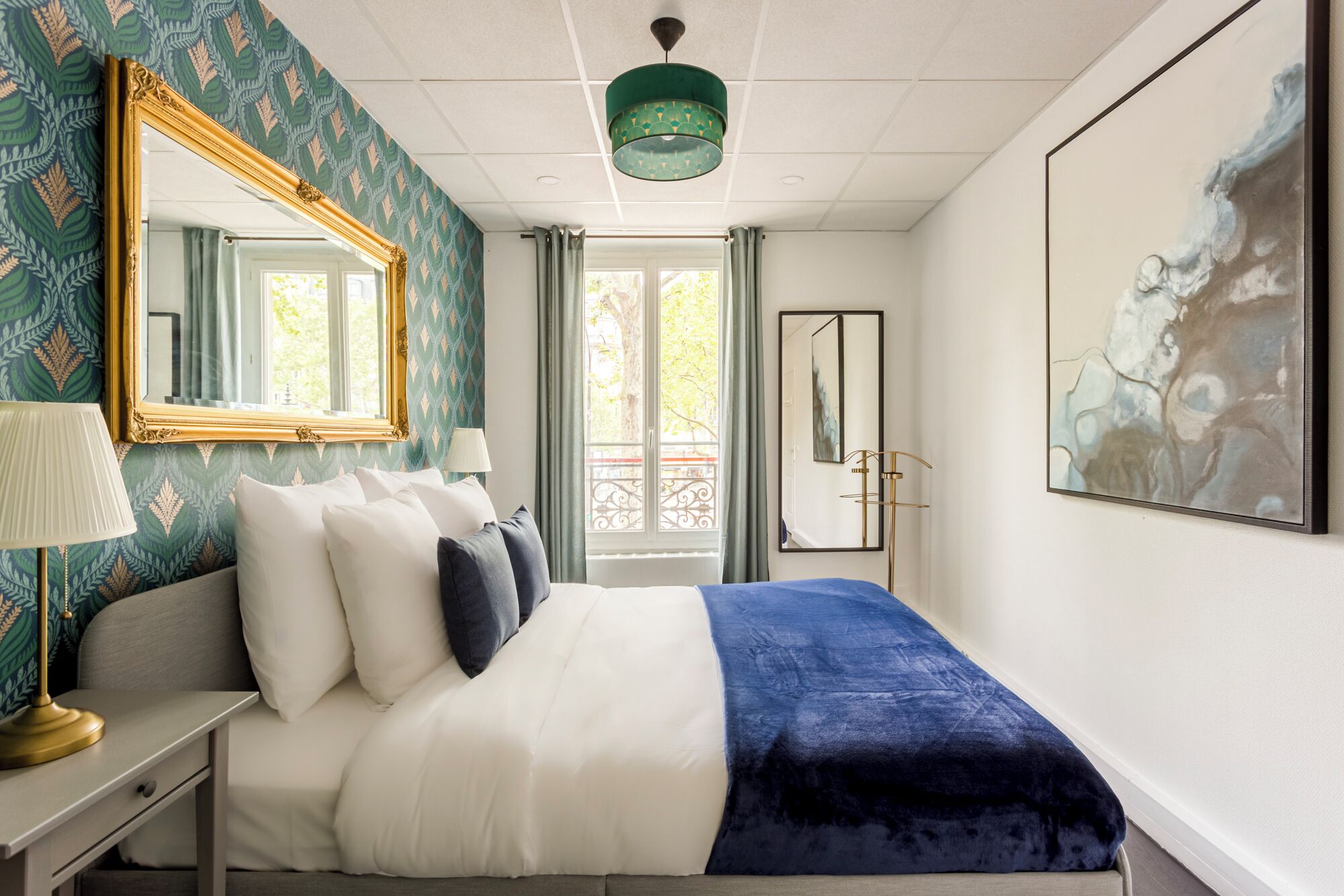 Una camera da letto con un letto, un comodino, una lampada, uno specchio e un quadro appeso al muro.