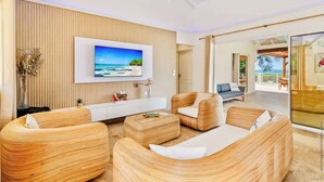Uma sala de estar moderna com uma televisão grande, móveis de vime e vista para o mar.