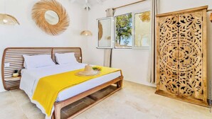 Quarto com cama, manta amarela, cabeceira de madeira, espelho, janela com vista e painel decorativo de madeira.