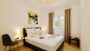 A neatly arranged bedroom with a bed, a chair, a bedside table, and a window with curtains. - T2 La Perle - Village Creole (Les Trois-Îlets)