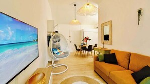 A modern living room with a large flat-screen TV, a hanging chair, a sofa, and a dining area with a table and chairs. - T2 La Perle - Village Creole (Les Trois-Îlets)