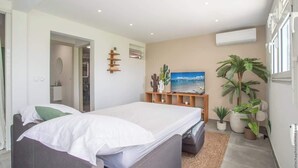 Een moderne slaapkamer met een bed, een televisie en een kleine plantenhoek.