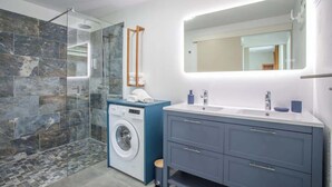 Een moderne badkamer met een douchecabine van glas, een wasmachine en een wastafel met een grote spiegel.