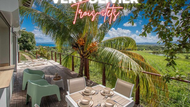 Een terras met een tafel voor vier personen, omringd door palmbomen en een mooi uitzicht.