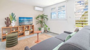 Een moderne woonkamer met een flatscreen televisie, een bank, een salontafel en diverse planten.