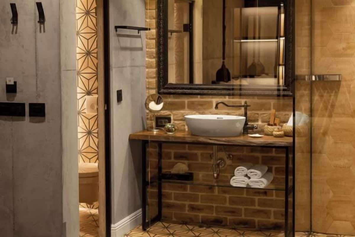 A bathroom with a stone wall, a glass shower enclosure, a white sink, and a mirror.