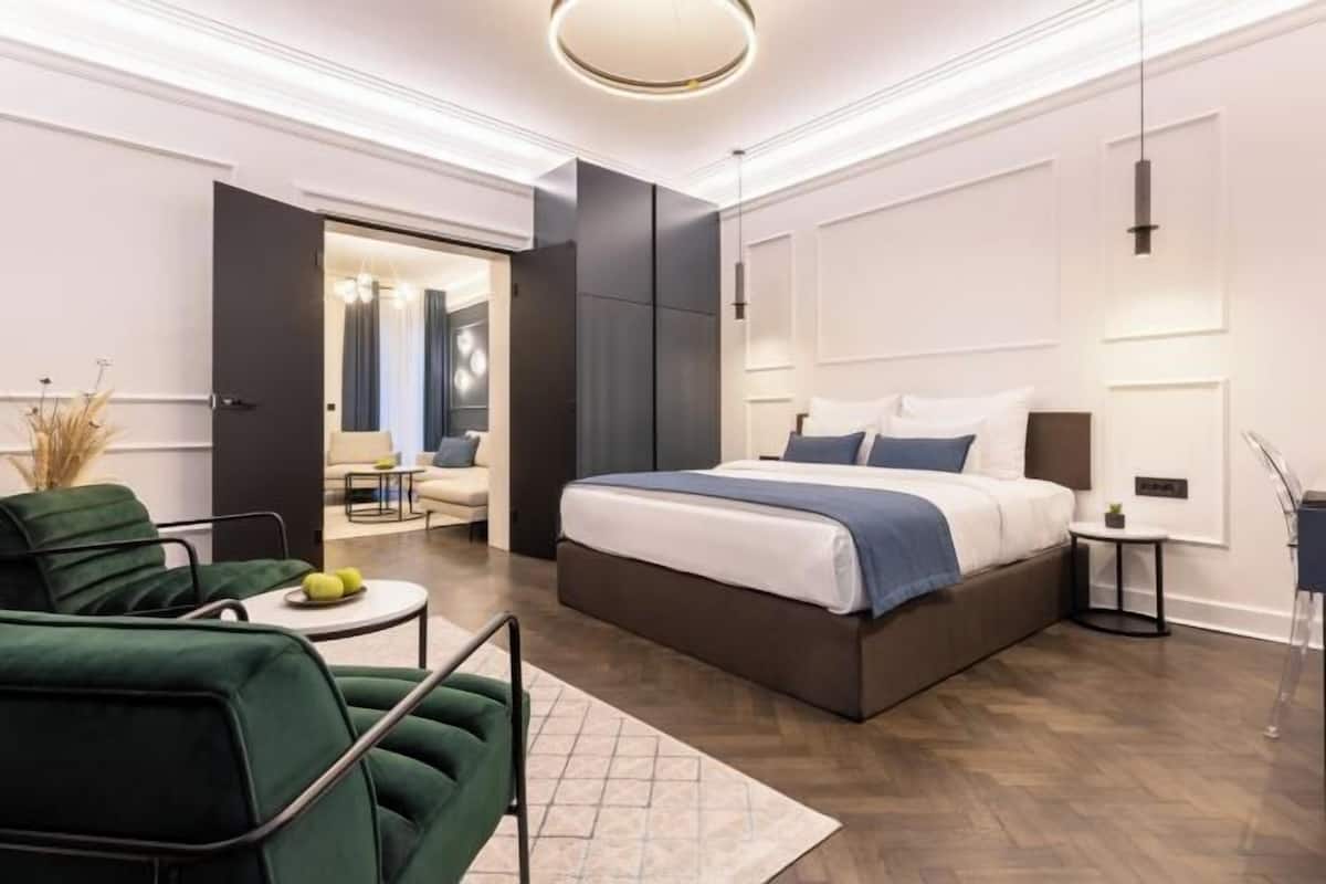 A modern bedroom with a large bed, a green armchair, a small round table, and a walk-in closet.